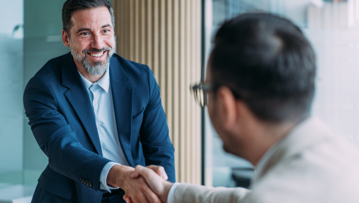 Two people shake hands across a conference room table. 