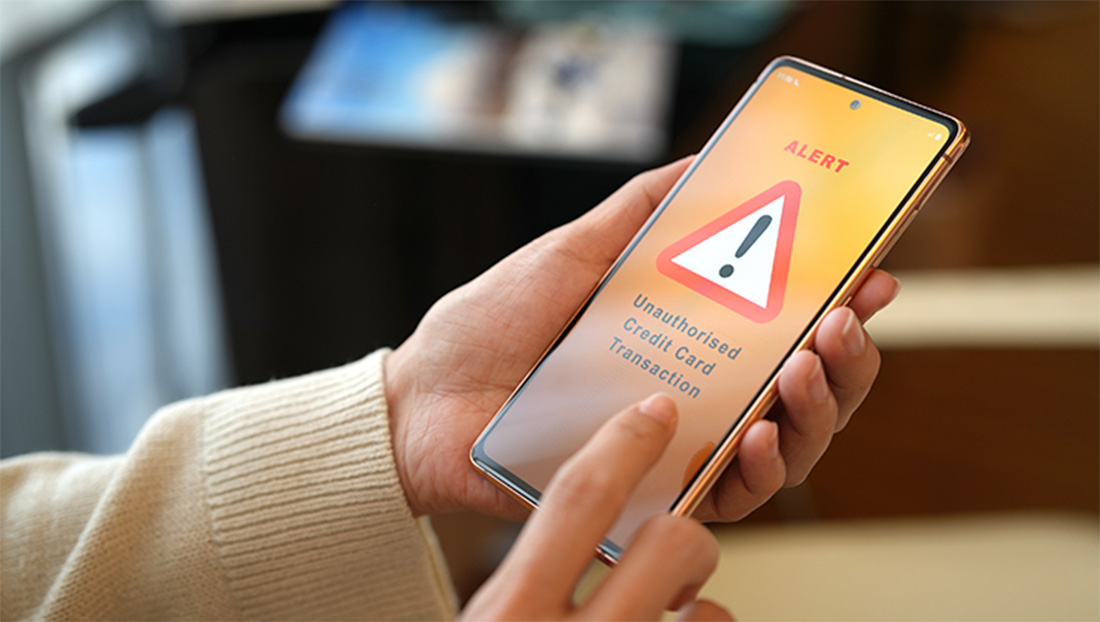 A close-up photo of a cell phone held by a person. On the screen is a yellow background with a large red and white alert symbol..