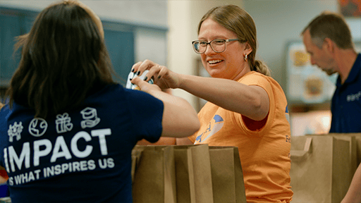 A woman wearing glasses passes a can of vegetables to another volunteer. 