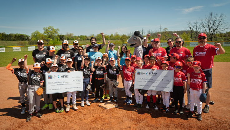 Volunteers and young baseball players stand together on the baseball diamond and pose for a photo. 