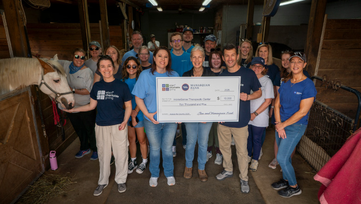 A group of volunteers stand in a horse barn holding a check.