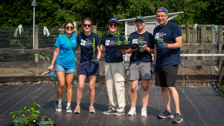 Volunteers stand together holding plants in a garden.