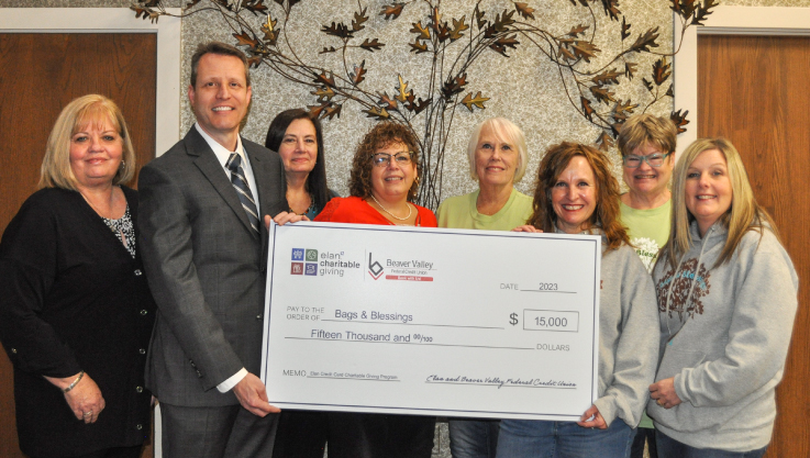 Eight adults hold a large check in front of a an indoor decoration that looks like a tree. 