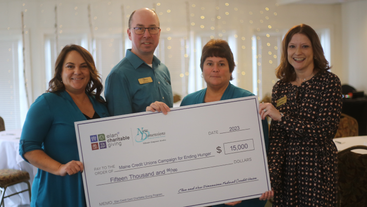 Four adults hold a check in a ballroom. Behind them are twinkle lights behind white curtains. 