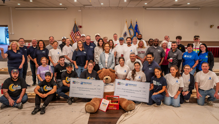 Volunteers stand for a group photo with two large promotional checks. 