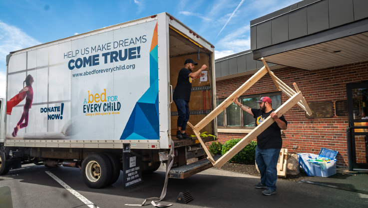 A volunteer helps load a child's bed frame on a delivery truck. 