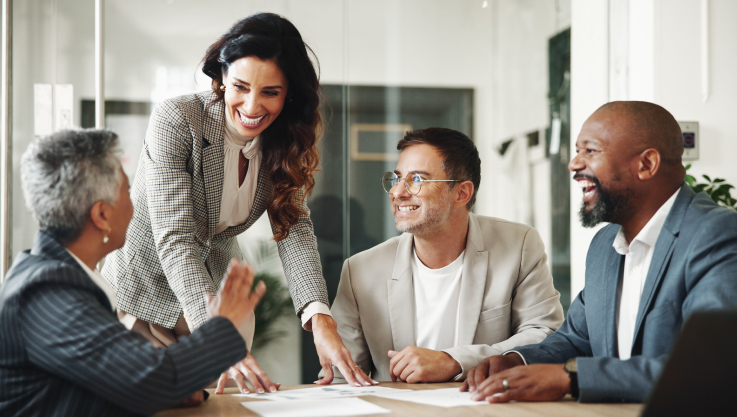 A group of business people gather at a conference table smiling. 