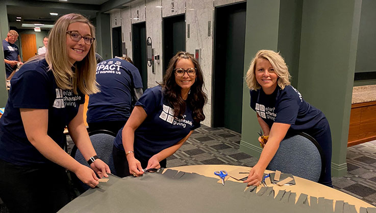 Three adults stand around a table cutting fabric to make a blanket. 