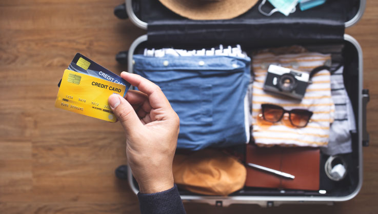 A person holds a credit card over a packed suitcase.