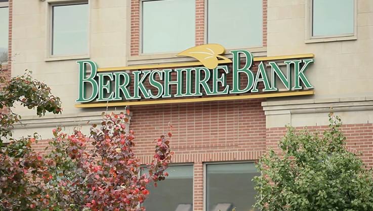 A brick building outdoors with some trees. The front of the building shows the Berkshire Bank logo.