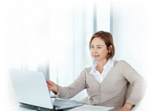 Woman in tan sweater uses her laptop in a bright airy room